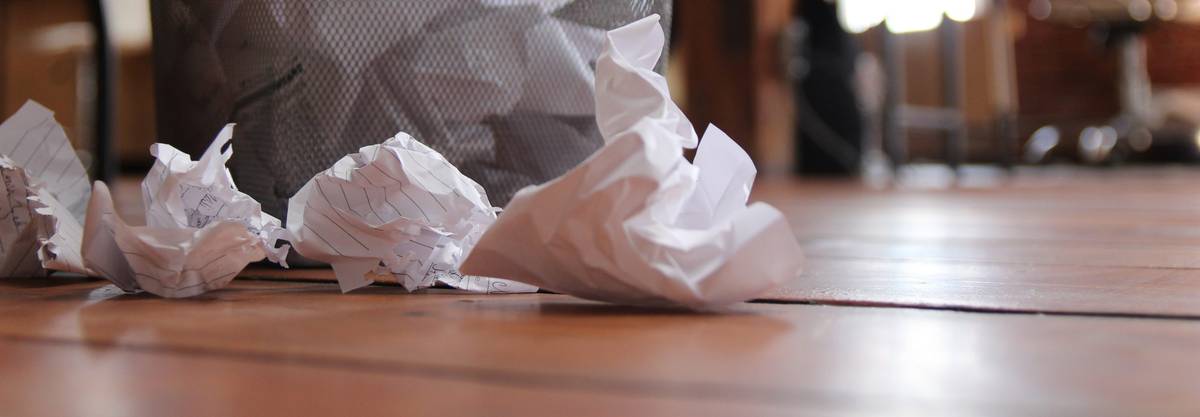 crumpled up paper on floor next to wastebasket