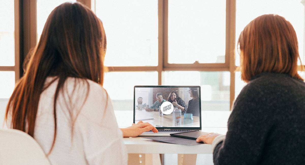 Two people looking at laptop with image of people in a meeting with 'Work With Purpose' overlay