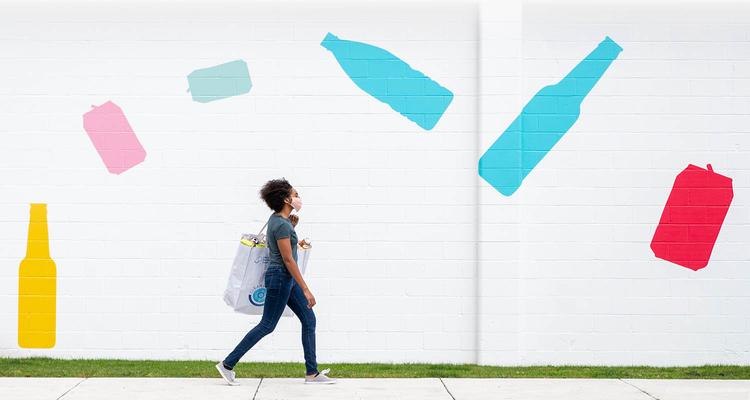 Woman Walking in Front of a Bottle and Can Mural