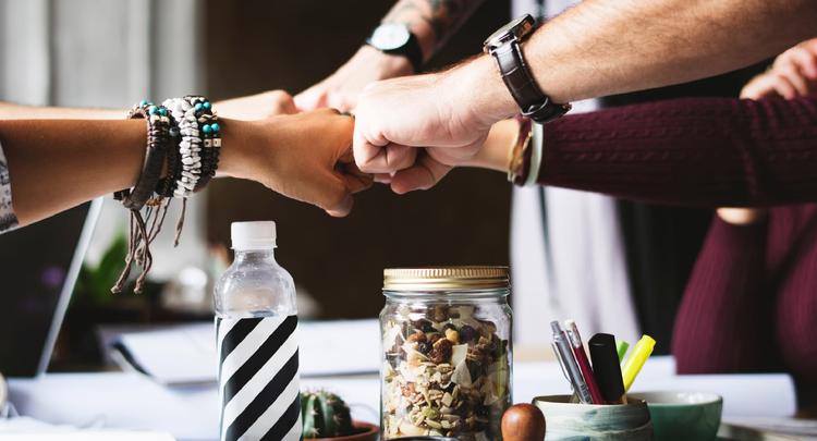 group of office people fist bumping over assorted desktop items and granola