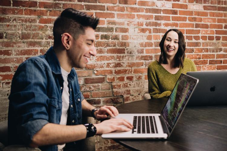 Smiling woman looking at smiling man typing at laptop