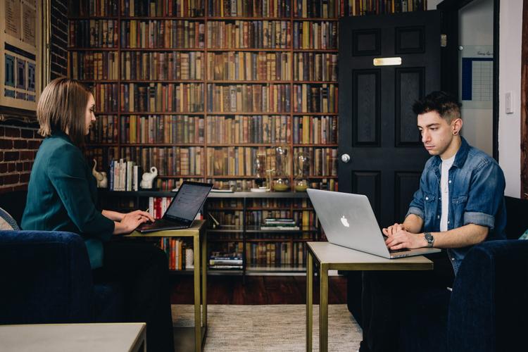 Two people sitting in a room typing at laptops