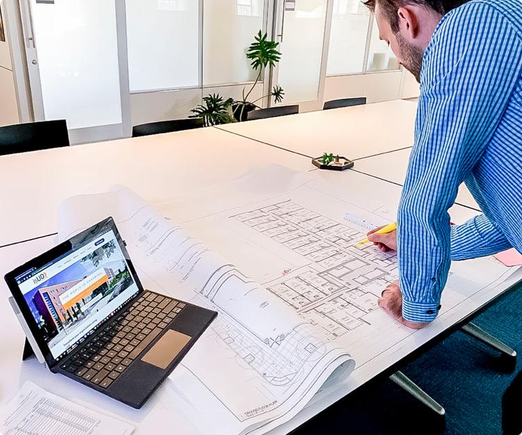 photo of man highlighting blueprint next to laptop