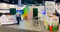 photo of the ODL exhibition booth, which shows a custom display counter, a monitor, an installation of colorful teeth, decorative grass hedges, a small seating booth