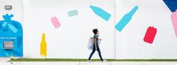 Woman Walking in Front of a Bottle and Can Mural